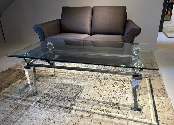 Eleganter Couchtisch aus Acryl und Glas von Kuatre, Ausstellungsstück auf Designteppich vor Frontansicht des Schröno Sofa Individual in braunviolettem JAB Anstoetz Stoff Vito 55