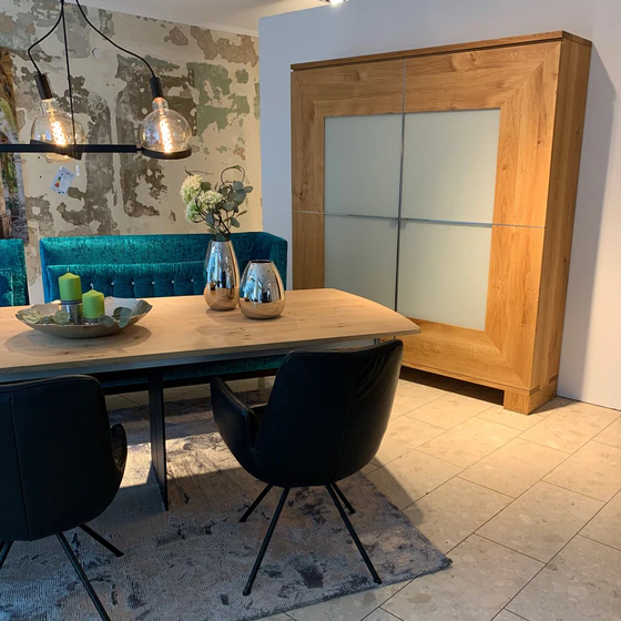 Großer Schrank Varus von Scholtissek in knorriger Eiche mit Glasfront in Sand matt – inszeniert im Essbereich mit Designmöbeln