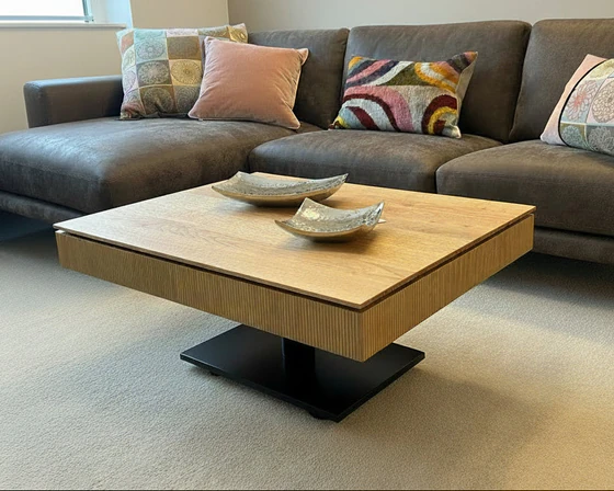 Höhenverstellbarer Couchtisch Ronald Schmitt Lignum K472 mit offener Ablage und verschiebbarer Schublade aus massiver gerillter Eiche, inszeniert in moderner Wohnzimmerumgebung.