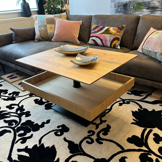 Höhenverstellbarer Couchtisch Ronald Schmitt Lignum K472 mit offener Ablage und verschiebbarer Schublade aus massiver gerillter Eiche, inszeniert in moderner Wohnzimmerumgebung.
