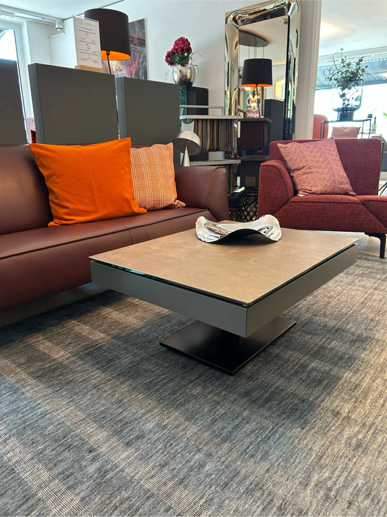 Moderner Ronald Schmitt Janas K 471 Couchtisch mit verschiebbarer Schublade und grauer Keramikplatte, präsentiert im Showroom von Zeppenfeld Wohn Evolution in Olpe in der Ausstellungsumgebung