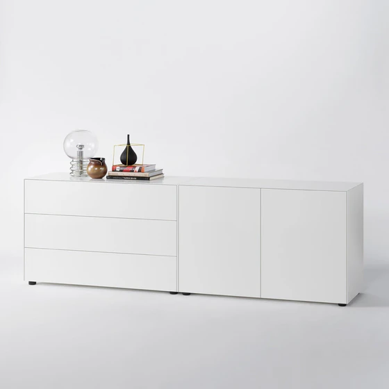 Weißes Sideboard mit klaren Linien, bestehend aus drei Schubladen links und zwei Türen rechts, mit schlichter Deko auf weißem Hintergrund.