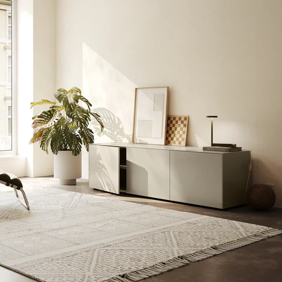 Piure Nex Pur Box 2020600 in Silk in heller Wohnumgebung – 3-türiges Sideboard unter Fenster, dekorativ inszeniert mit Kunst, Lampe und Pflanzen.