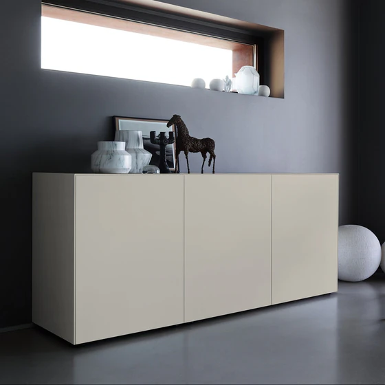 Elegantes Sideboard Piure 2020500 in Farbe Silk, modern inszeniert vor dunkler Wand mit Skulpturen und Vasen