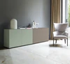 Moderne Sideboardkombination mit Piure Nex Pur Box Türmodul in Salbeigrün links und Schubkastenelement in warmem Taupegrau rechts, in heller Wohnumgebung mit grauer Wand und Design-Sessel.