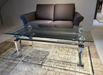 Eleganter Couchtisch aus Acryl und Glas von Kuatre, Ausstellungsstück auf Designteppich vor Frontansicht des Schröno Sofa Individual in braunviolettem JAB Anstoetz Stoff Vito 55