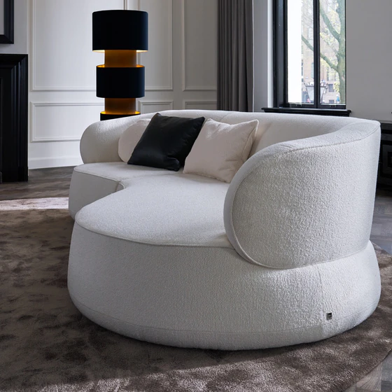 Detailansicht des Bielefelder Werkstätten Sofa Nimbo von rechts mit großzügiger geschwungener Sitzfläche, weich gerundeter Armlehne und cremeweißem Strukturstoff.