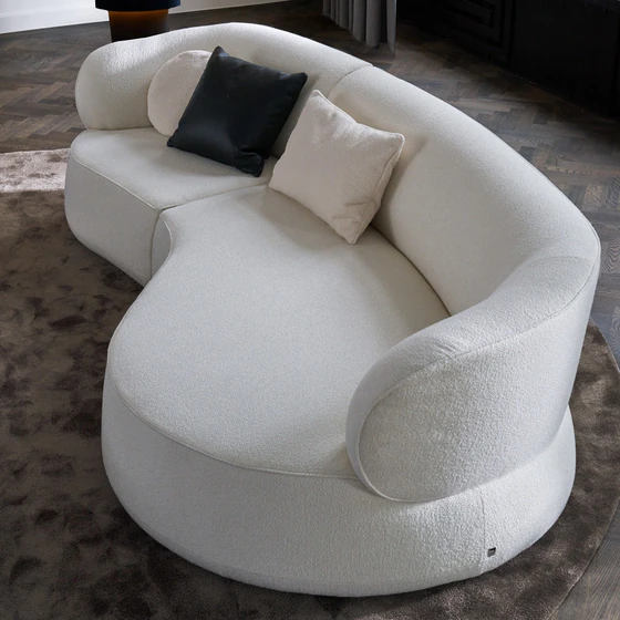 Detailansicht des Bielefelder Werkstätten Sofa Nimbo von oben mit großzügiger geschwungener Sitzfläche, weich gerundeter Armlehne und cremeweißem Strukturstoff mit Dekokissen