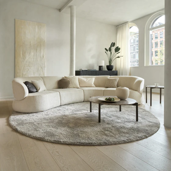 Modulares Sofa Nimbo von Bielefelder Werkstätten in cremeweißem Stoff in einem hellen Wohnraum mit runder Teppichfläche, Couchtisch und organisch geschwungener Form.
